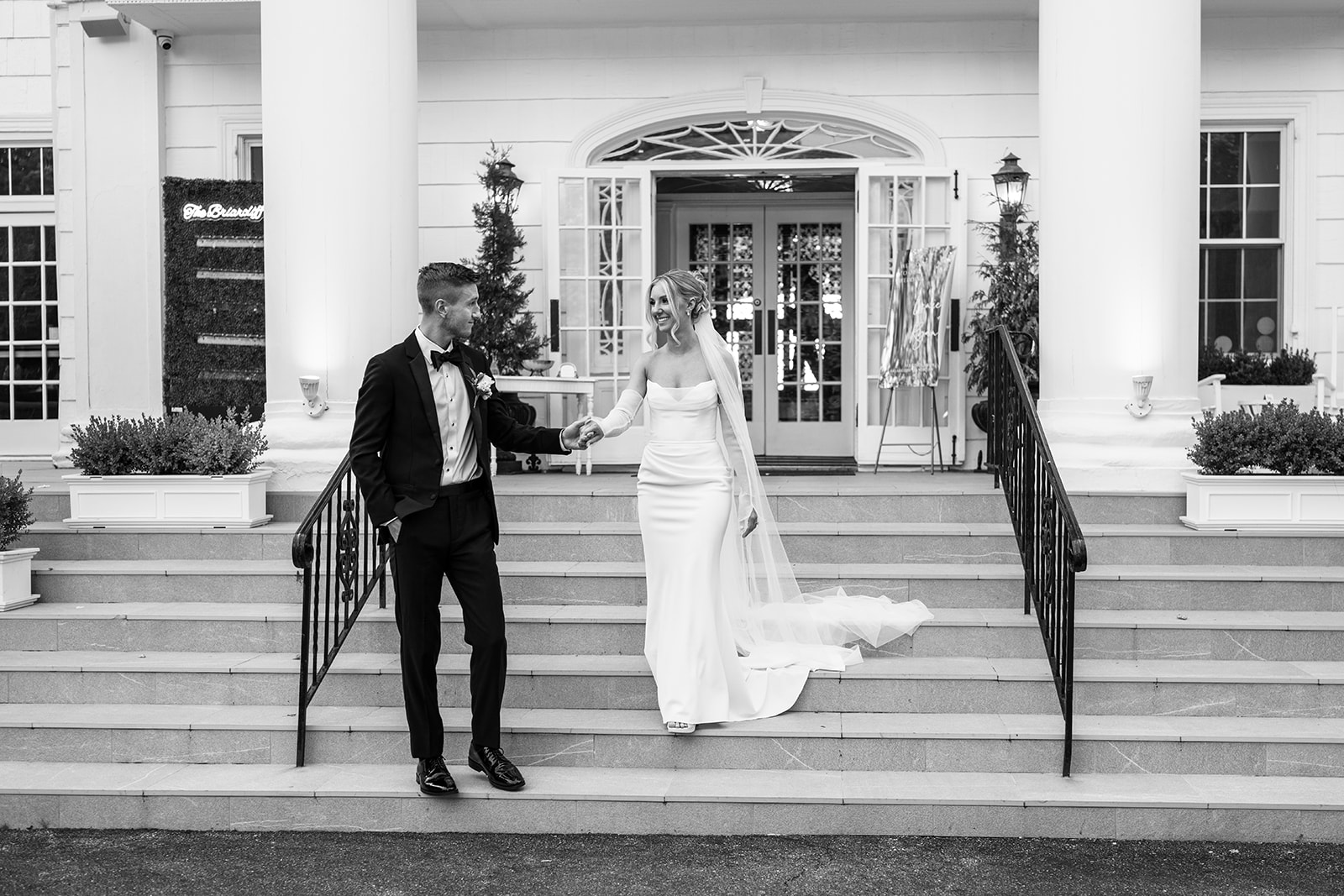 Black and white portrait of the bride and groom smiling as they walk down the grand stairs together.